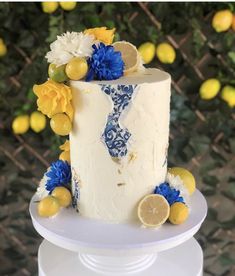 a white cake with blue and yellow flowers on top is sitting on a table next to lemons