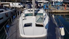 a sailboat docked at a marina with other boats in the water and people standing on it