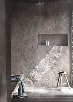 a bathroom with concrete walls and stools in front of the shower area, along with a towel on the floor