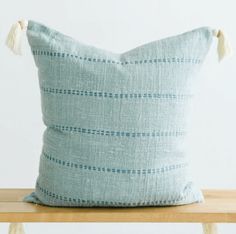 a blue pillow sitting on top of a wooden table next to a white wall with tassels