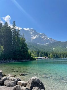 a lake surrounded by mountains and trees with clear water in the foreground on a sunny day