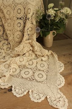 a white crocheted blanket sitting on top of a wooden floor next to a potted plant