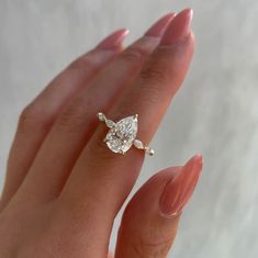 a woman's hand holding an engagement ring with a pear shaped diamond on it