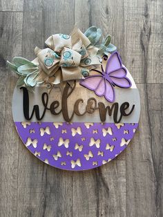 a welcome sign with butterflies and bows on it sitting on top of a wooden floor