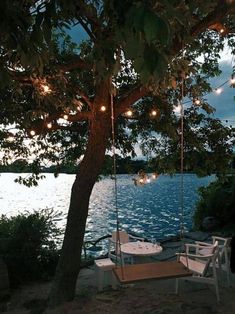 there is a table and chairs on the beach by the water with lights strung from it