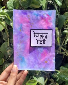 a hand holding up a piece of paper with the words happy holi written on it