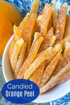 candied orange peels in a white bowl next to an orange on a blue and white tablecloth