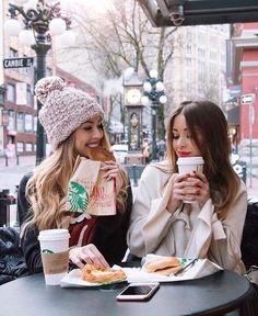 two women sitting at a table drinking coffee and eating