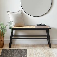 a black bench with a white pillow on it next to a plant and a round mirror