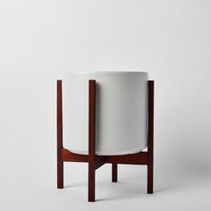 a white planter sitting on top of a wooden stand in front of a wall