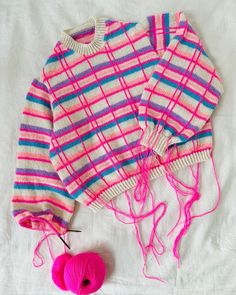 a sweater and ball of yarn are laying on a white sheet next to the knitting needles