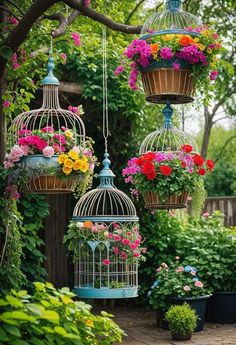 four birdcages with flowers hanging from them in the middle of a garden area