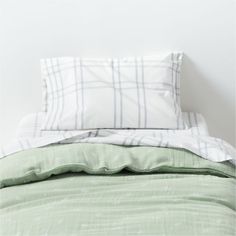 an unmade bed with green sheets and pillows