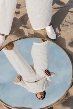 the reflection of a person in a round mirror on top of some sand and water