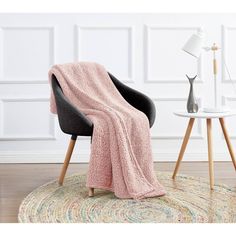 a blue blanket sitting on top of a chair next to a white table and lamp