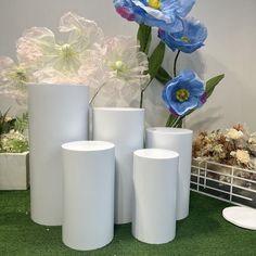 several white vases sitting on top of a grass covered ground next to flowers and plants