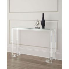 a clear console table with a black vase on top and white walls in the background