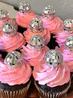 there are many cupcakes with pink frosting and disco ball decorations on them