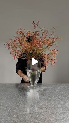 a man holding a vase with flowers in it on top of a marble countertop