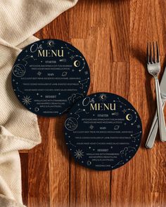 two black menu cards sitting on top of a wooden table next to a fork and knife