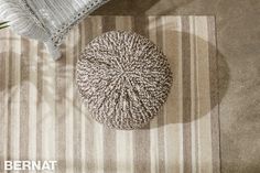 a small round poufce sits on the floor next to a striped rug and pillow