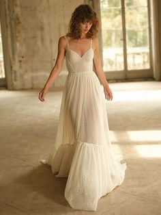 a woman in a white dress is walking through an empty room with large windows and brick walls