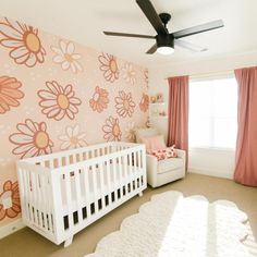 a baby's room with pink and orange flowers on the wall, white crib, and large window