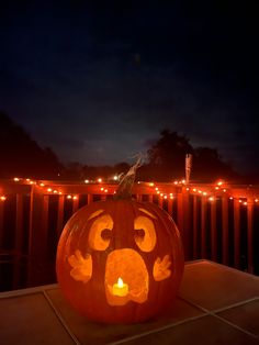 a carved pumpkin sitting on top of a porch next to a fence with lights around it