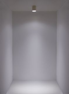 an empty white room with light coming in from the ceiling and lights on either side