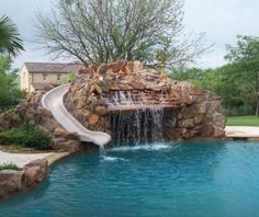 a pool with a slide in it next to a tree and water features on the side