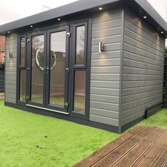 a small gray building sitting on top of a grass covered field next to a wooden deck