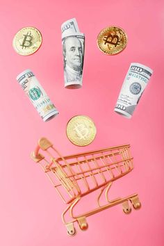 a shopping cart filled with money sitting on top of a pink table next to coins