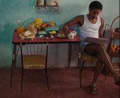 a man sitting at a table with food on it and reading a book in front of him