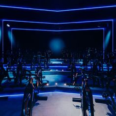 an indoor gym with rows of stationary bikes and blue lights on the ceiling, all lit up