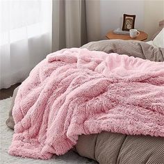 a bed with a pink blanket on top of it next to a night stand and window