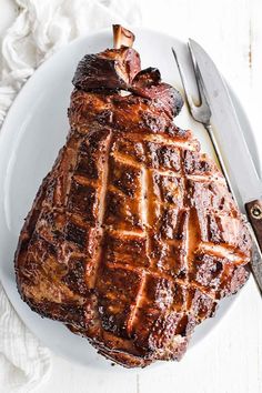 a piece of meat on a white plate with a knife and fork next to it