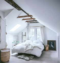 an attic bedroom with white bedding and wooden beams on the ceiling is decorated in natural materials