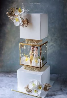 three tiered wedding cake decorated with white flowers and gold trimmings on top