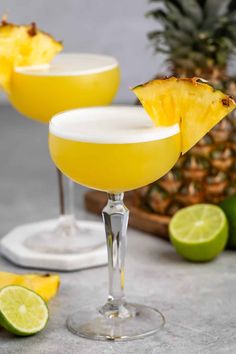 two margaritas with pineapple garnish on the rim and one in front