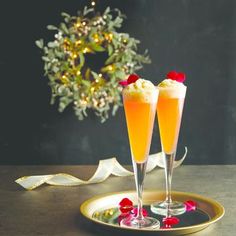 two glasses filled with champagne sitting on top of a plate next to a christmas wreath