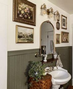 a white sink sitting under a bathroom mirror next to a wooden table with flowers on it