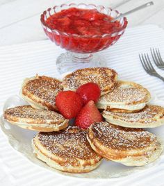 pancakes with powdered sugar and strawberries are arranged on a plate next to a bowl of strawberries