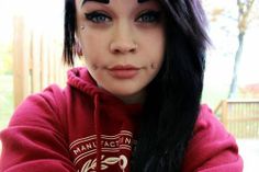 a woman with black hair and piercings on her face, wearing a red hoodie