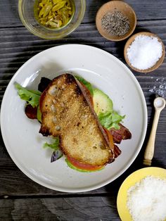 a white plate topped with a sandwich next to bowls of seasoning and spoons