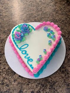 a heart shaped cake sitting on top of a white plate with blue and pink frosting