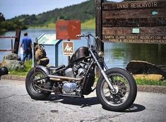 a motorcycle parked next to a sign near the water and people walking around in the background