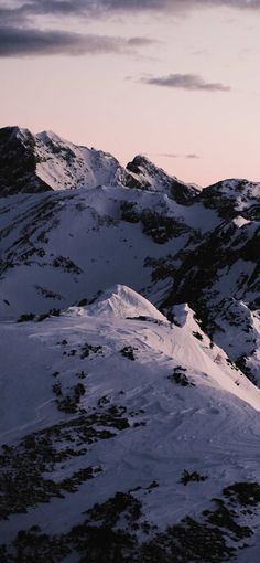 snow covered mountains under a purple sky with clouds in the foreground and one person on skis