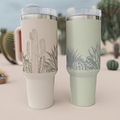 two coffee cups sitting next to each other on top of a sandy beach covered in cacti