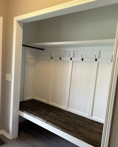 an empty white mud room with wooden bench and coat racks on the wall, along with several hooks