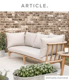 a couch sitting on top of a white rug next to a potted plant in front of a brick wall